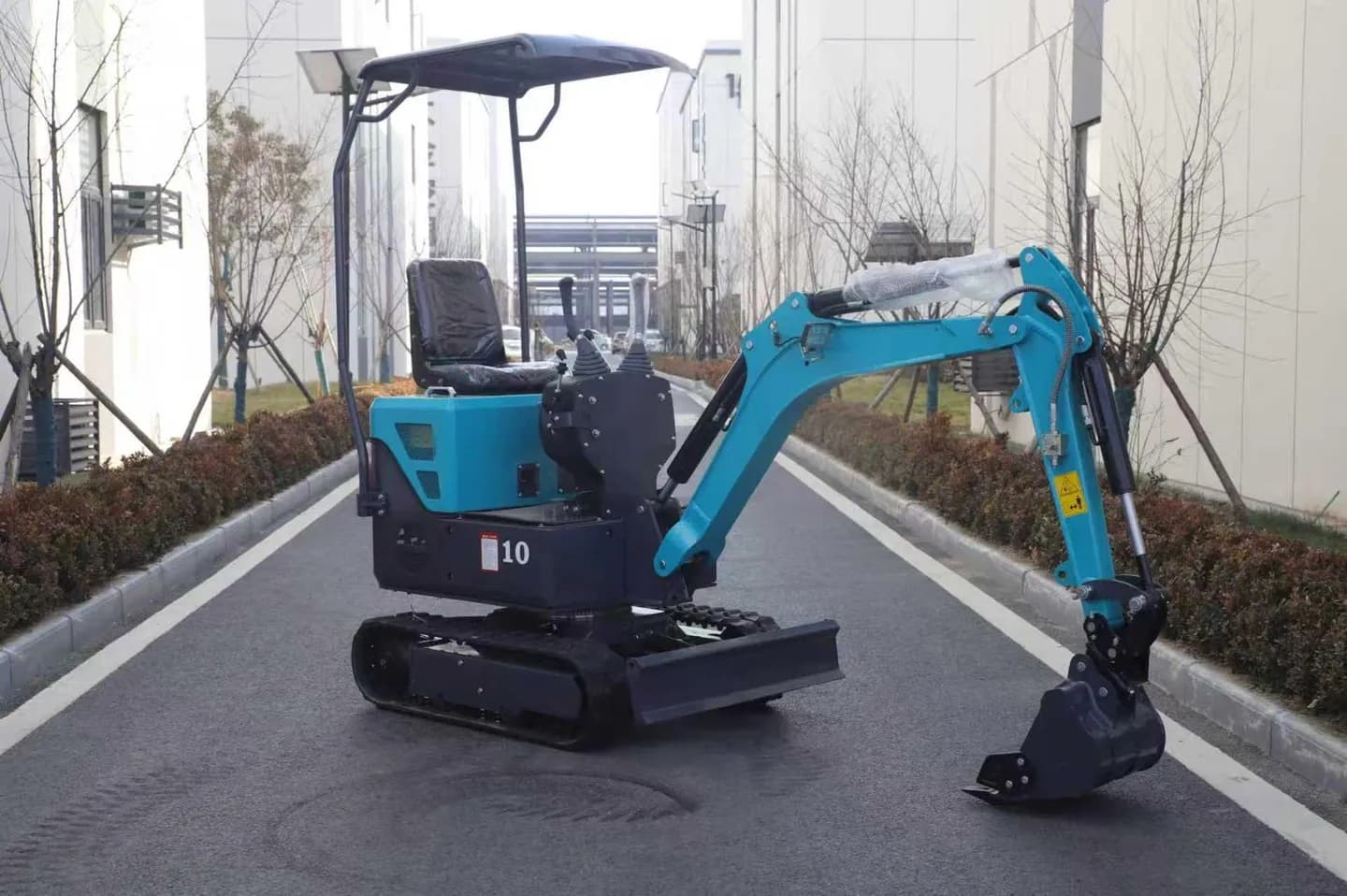 Blue compact tracked excavator with canopy, digging bucket and front blade, side view