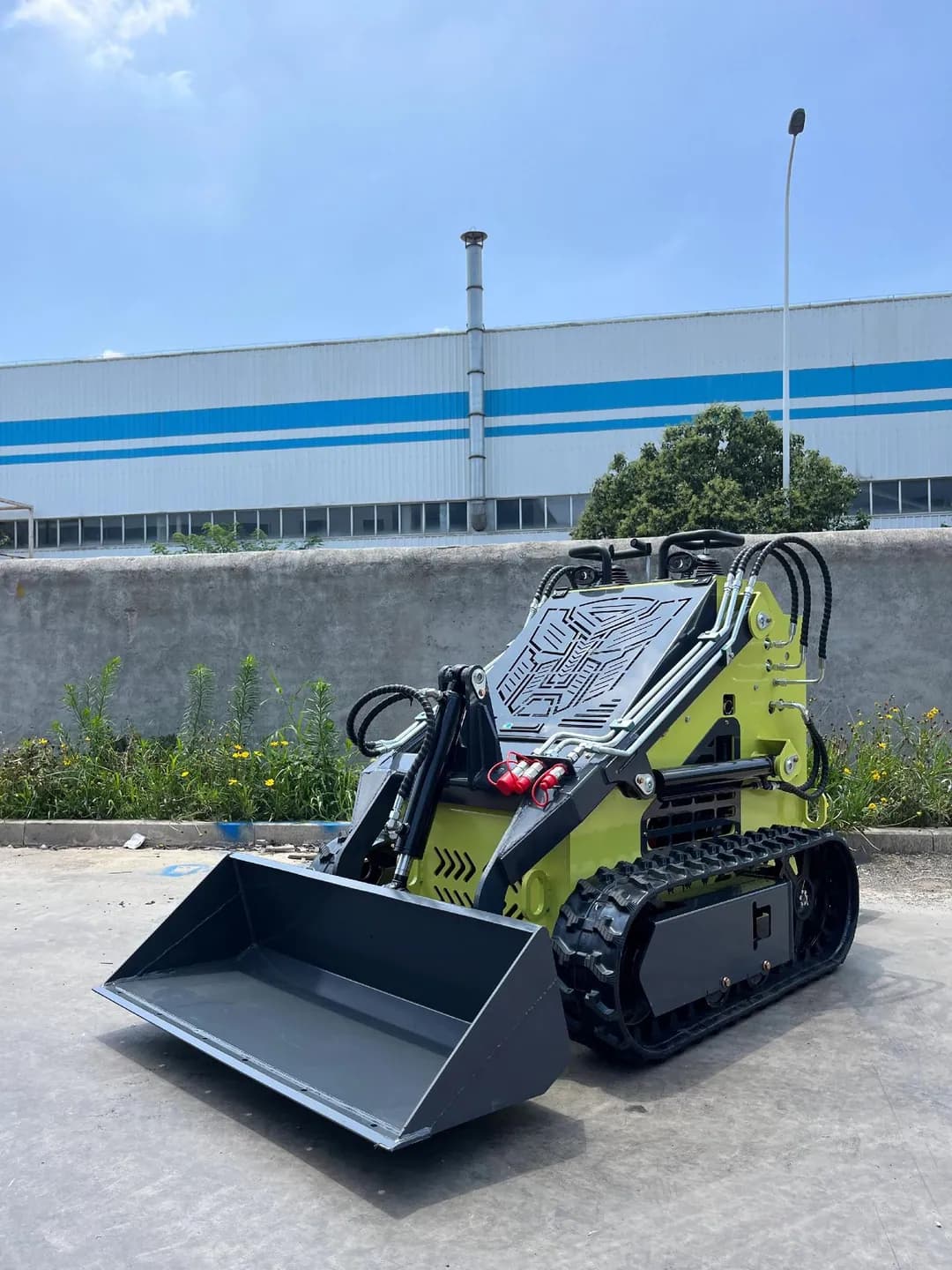 Pale green stand-on tracked loader with bucket, front three-quarter view