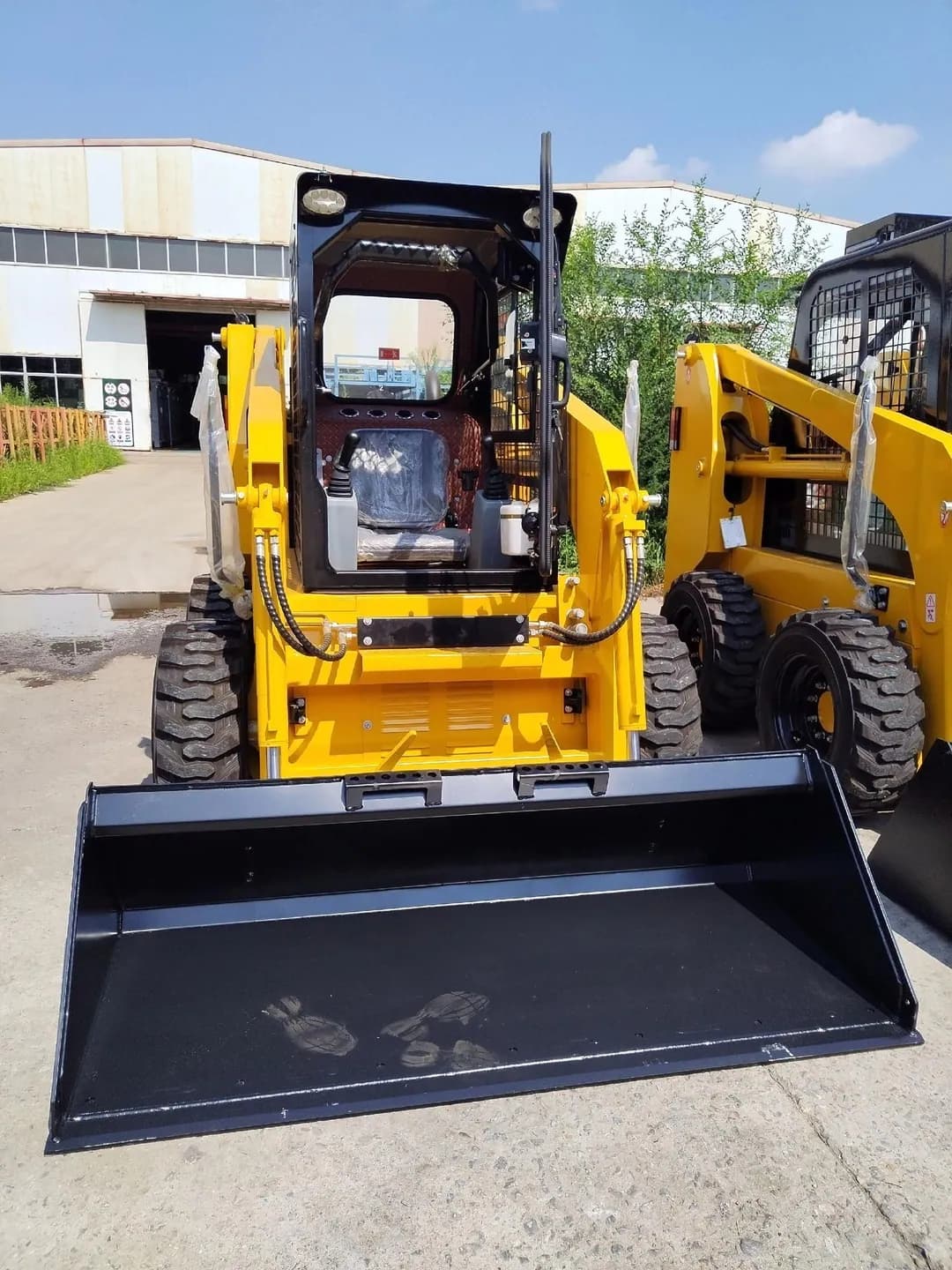 Front of a yellow wheeled skid steer loader showing its operator area and bucket