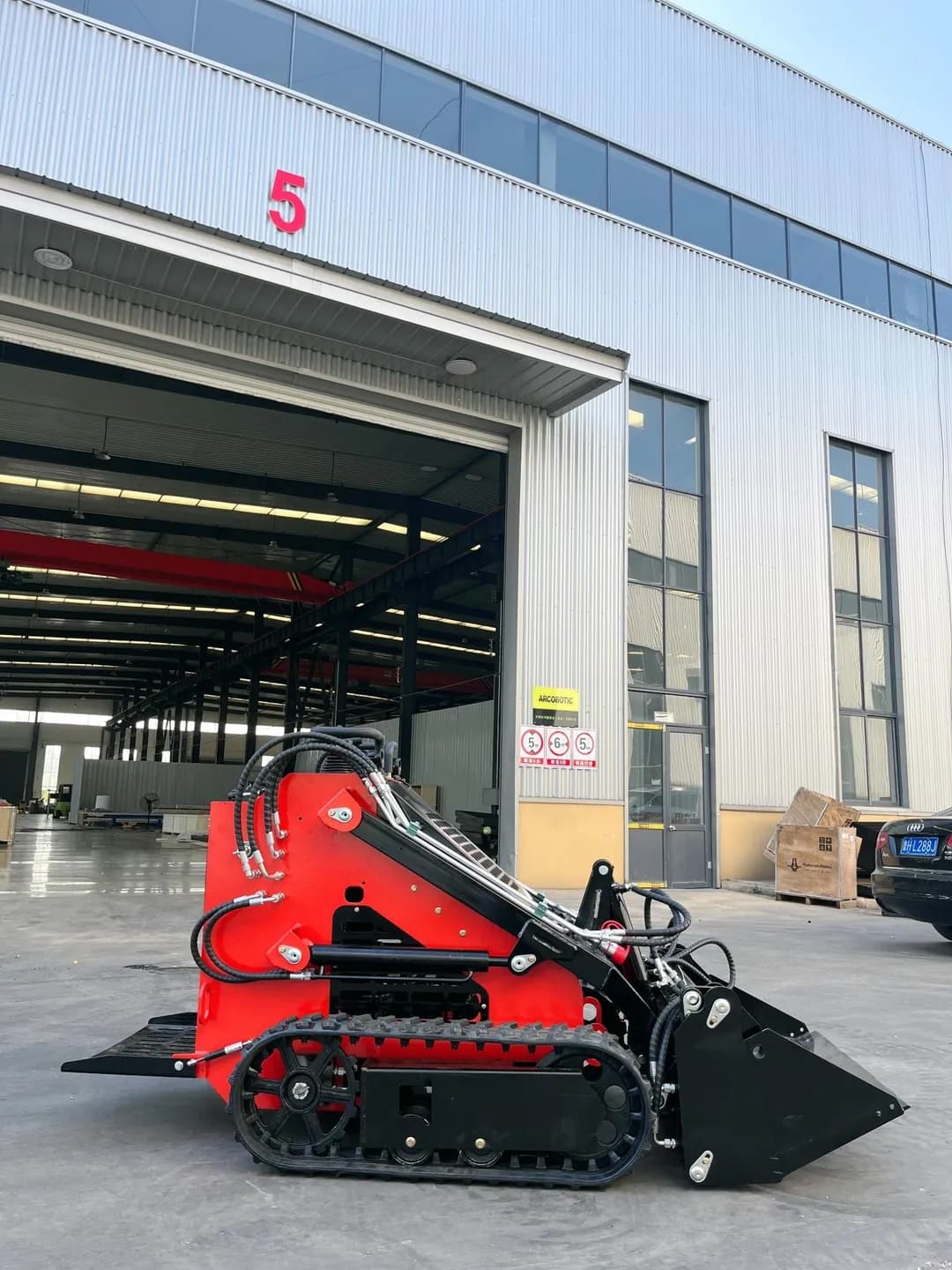 Red stand-on tracked loader with its bucket on the ground, full side view