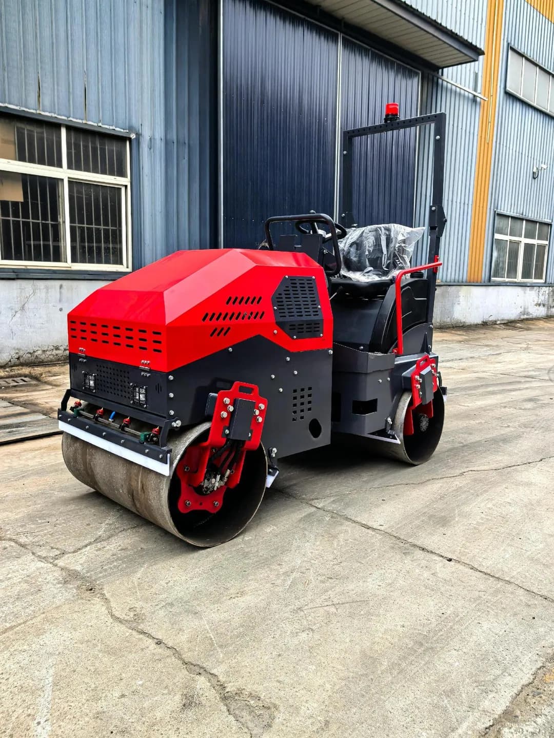 Red ride-on road roller showing its front drum and operator area