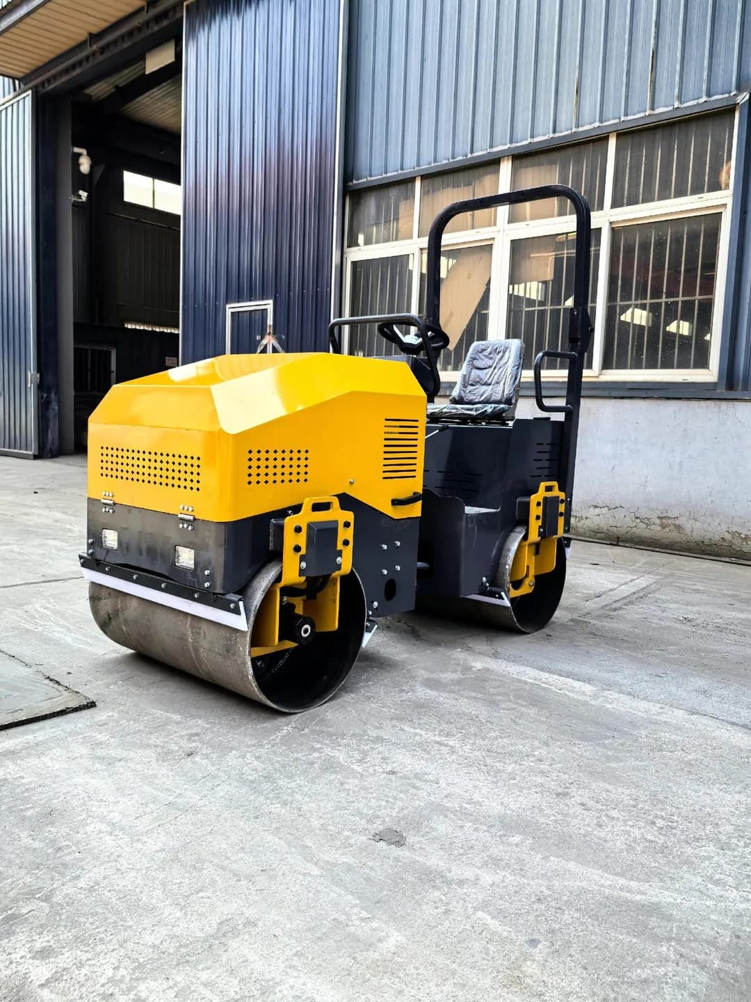 Yellow ride-on twin-drum roller with open seat, front three-quarter view outdoors