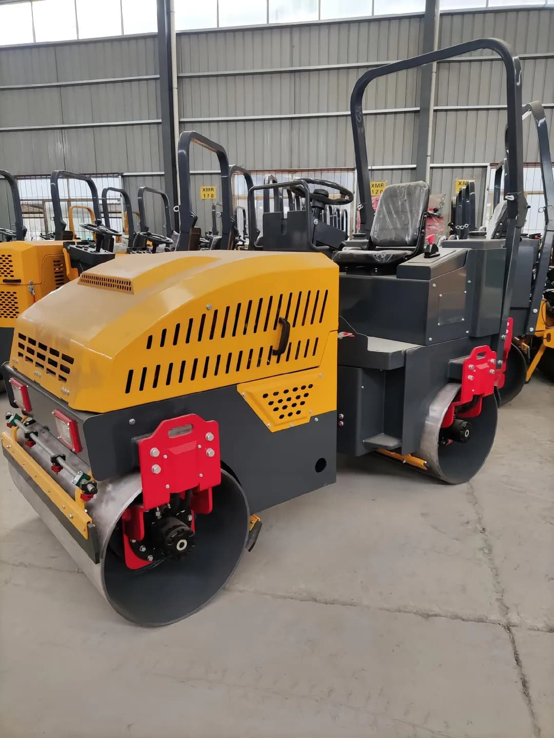 Yellow ride-on twin-drum roller inside a workshop, front three-quarter view