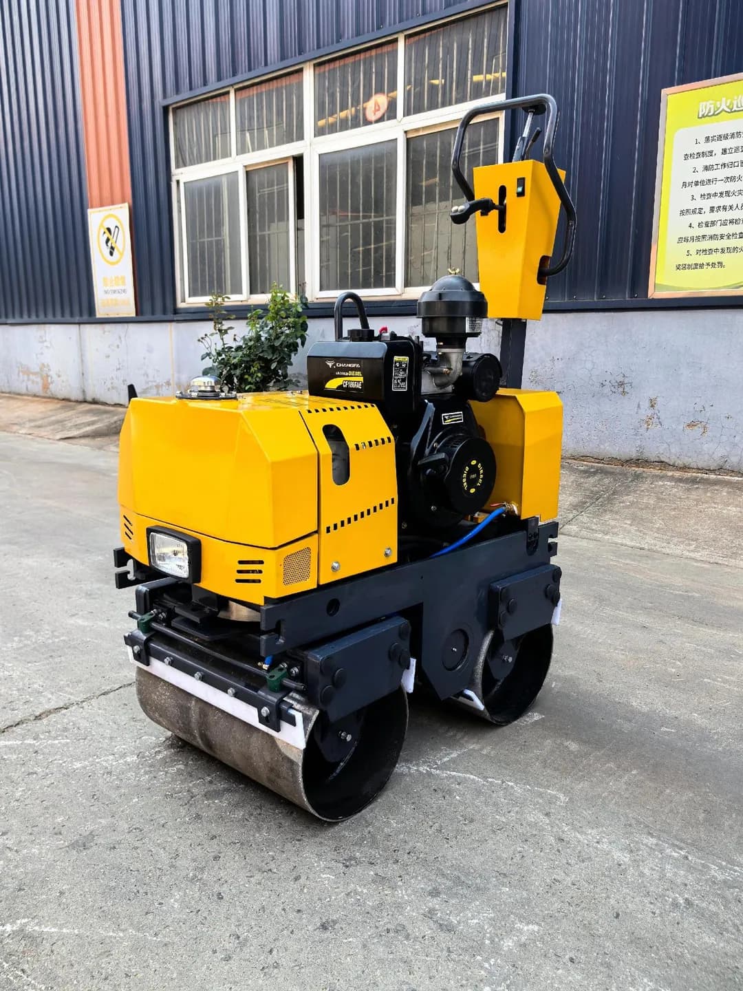 Yellow walk-behind roller with exposed engine and upright control handle, front view