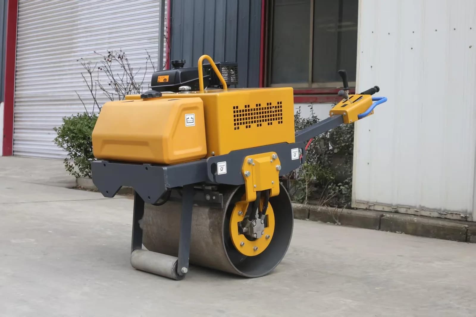 Yellow walk-behind road roller with steel drum and long control handle, side view